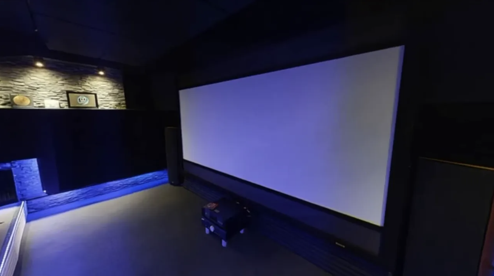 Dunkler Kinoraum mit großer Leinwand, blauer Bodenbeleuchtung und zwei Sitzreihen